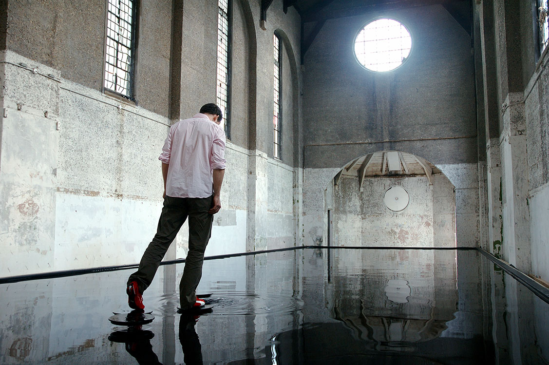 Bridge at Dilston Grove. A man walks over a room filled with water on mechanical steps.