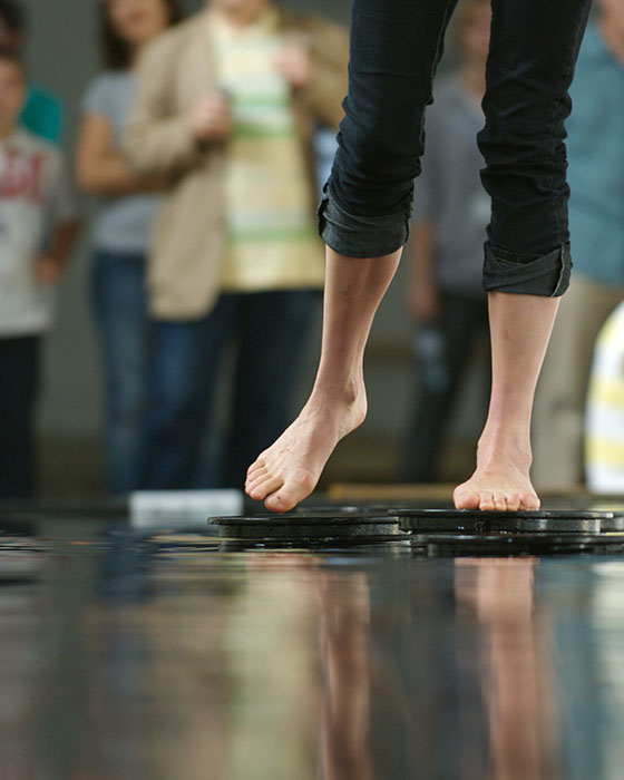 Bridge at Dilston Grove. A woman walks over a room filled with water on mechanical steps.