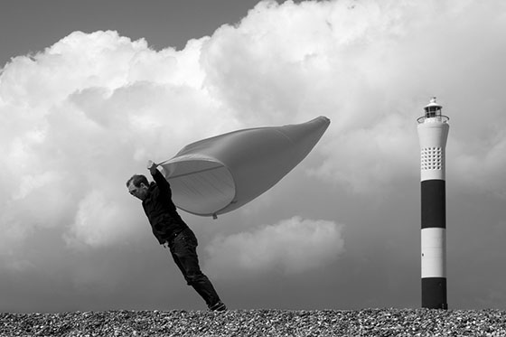 A man lies exhausted on the ground on a hillside, the wind funnel is empty and flapping around.